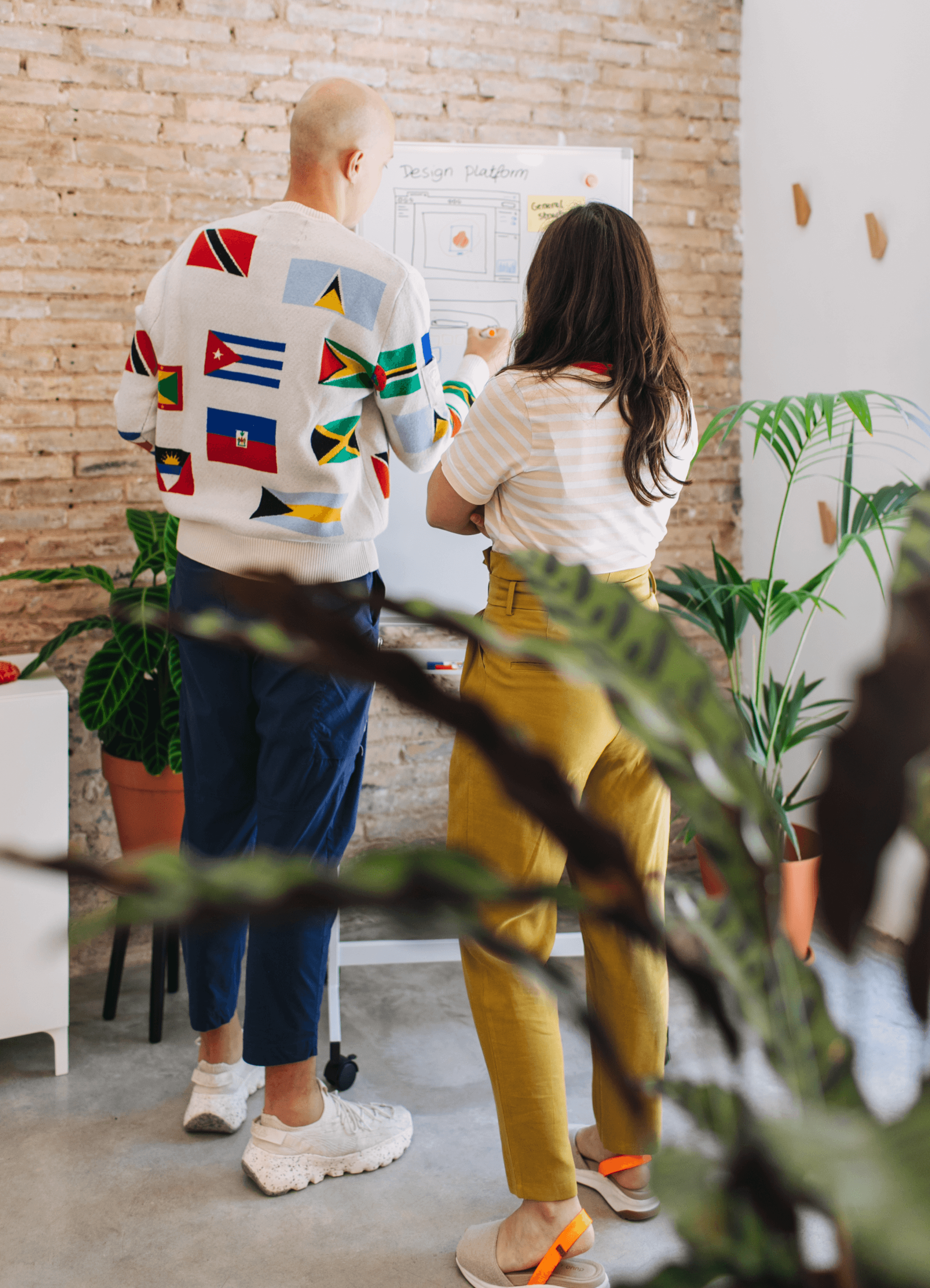 Two designers drawing wireframes on a whiteboard with plants around them.