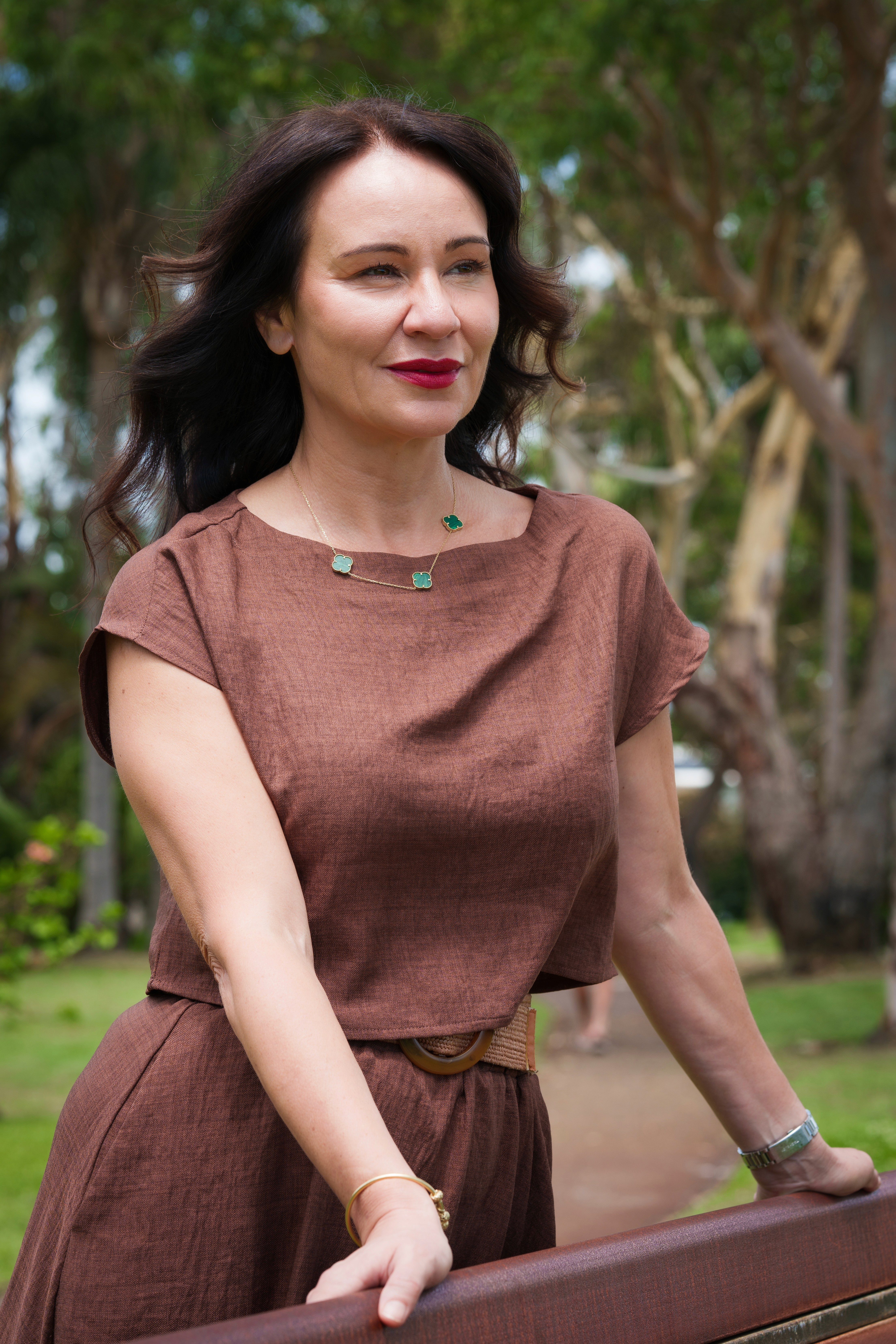 Dr. Bonnie Hawthorne with dark hair poses outdoors in a brown dress, smiling against a backdrop of greenery.