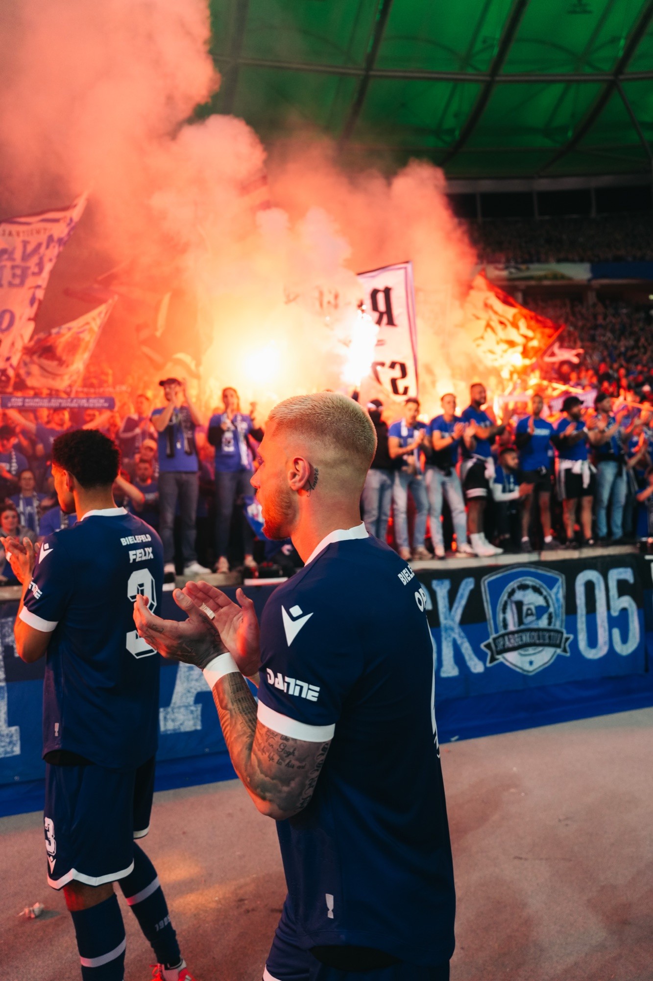 Spieler klatschen vor der Fankurve mit Pyrotechnik