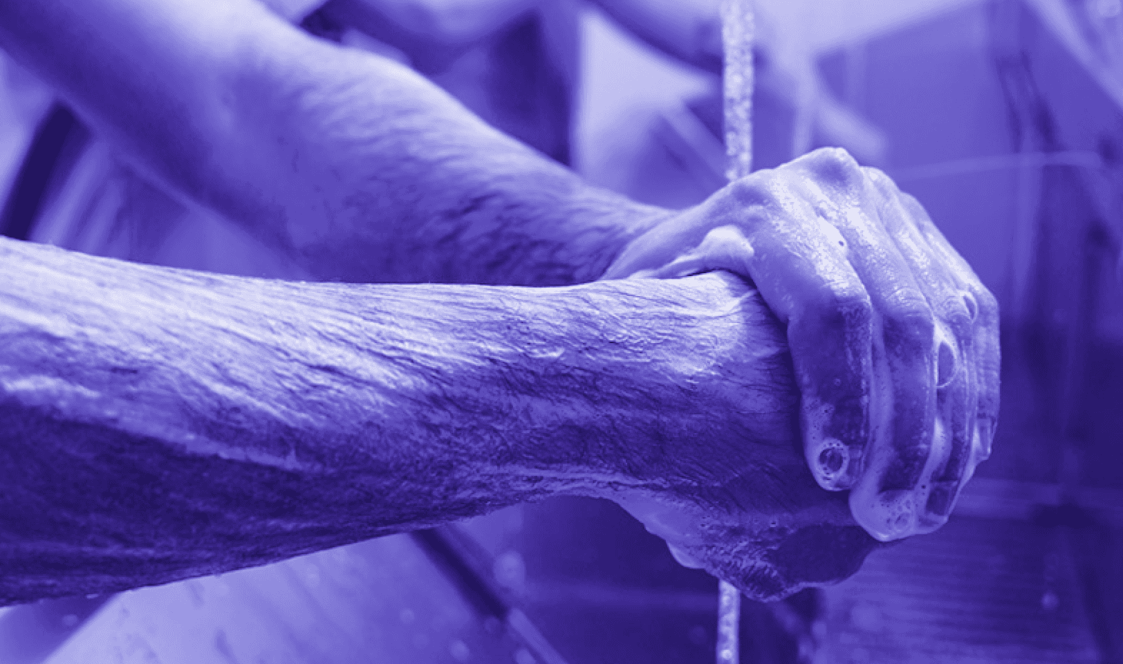 Imagem, em tons de roxo, de um profissional da saúde lavando as mãos.