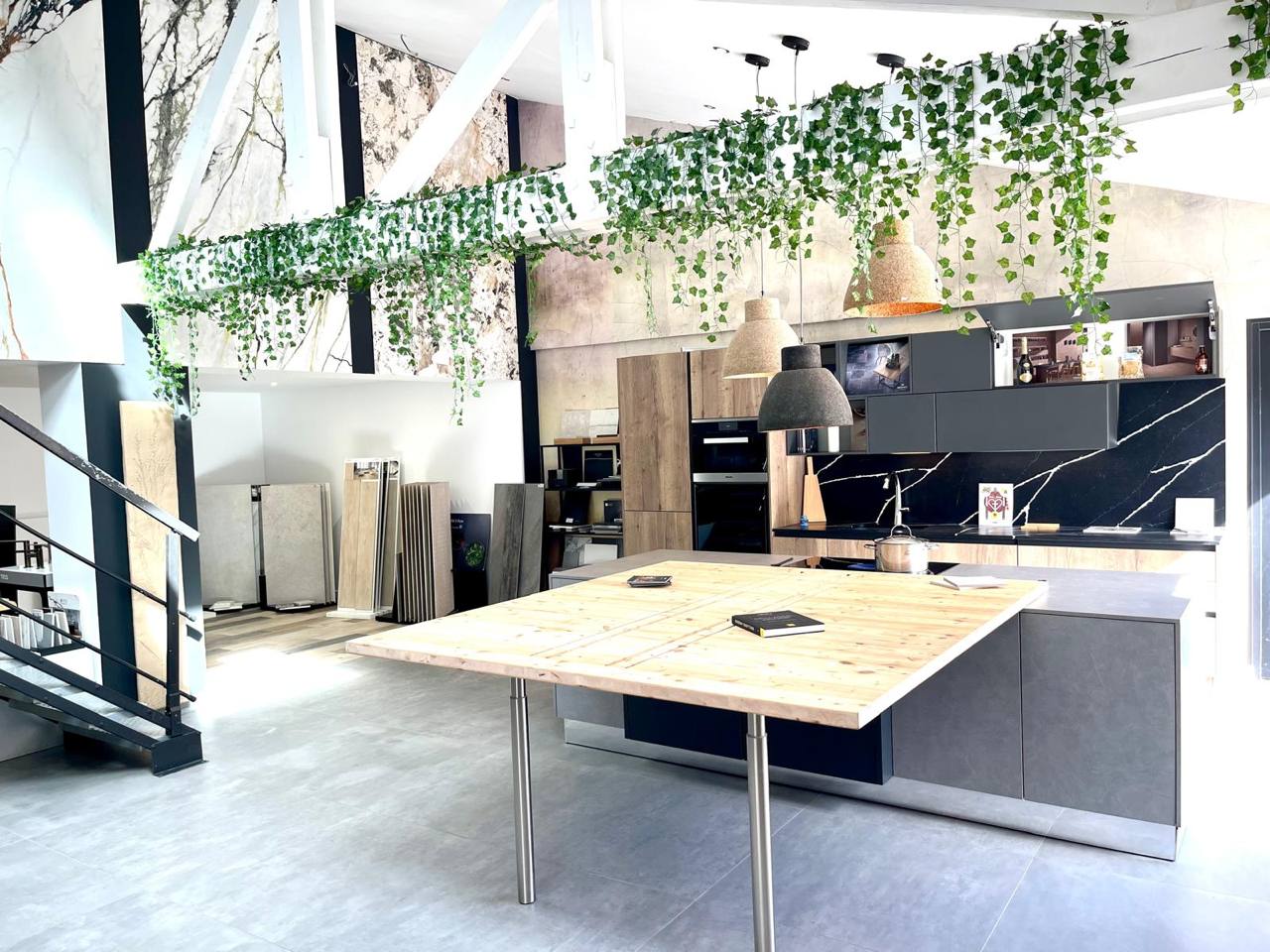 Cuisine exposition moderne Seine-et-Marne avec îlot bois, armoires noires et plantes suspendues, showroom design contemporain.