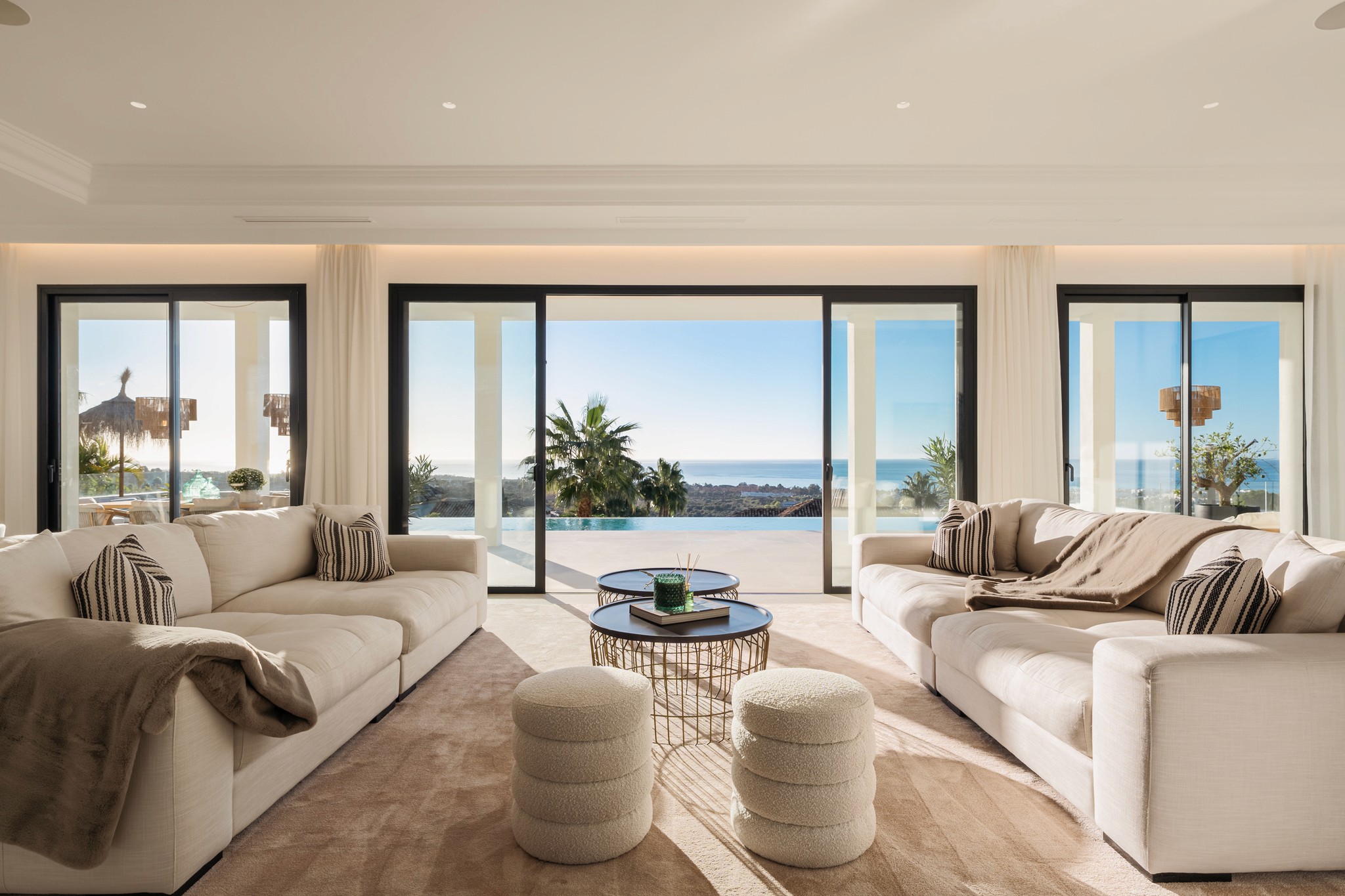 Salon moderne avec vue mer, grandes baies vitrées et mobilier beige.