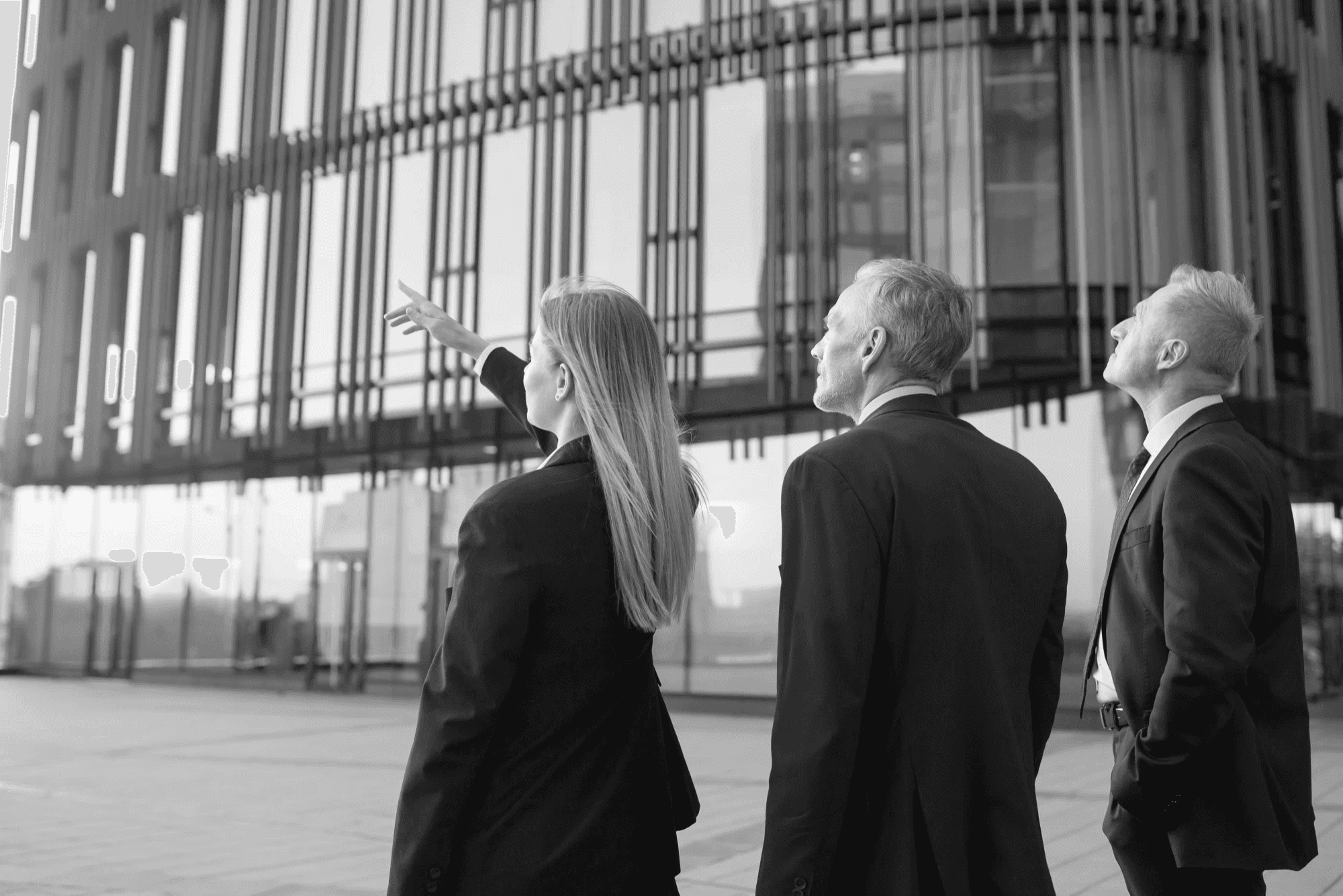 “Three business leaders outside a modern building, looking up and discussing architecture in black and white.