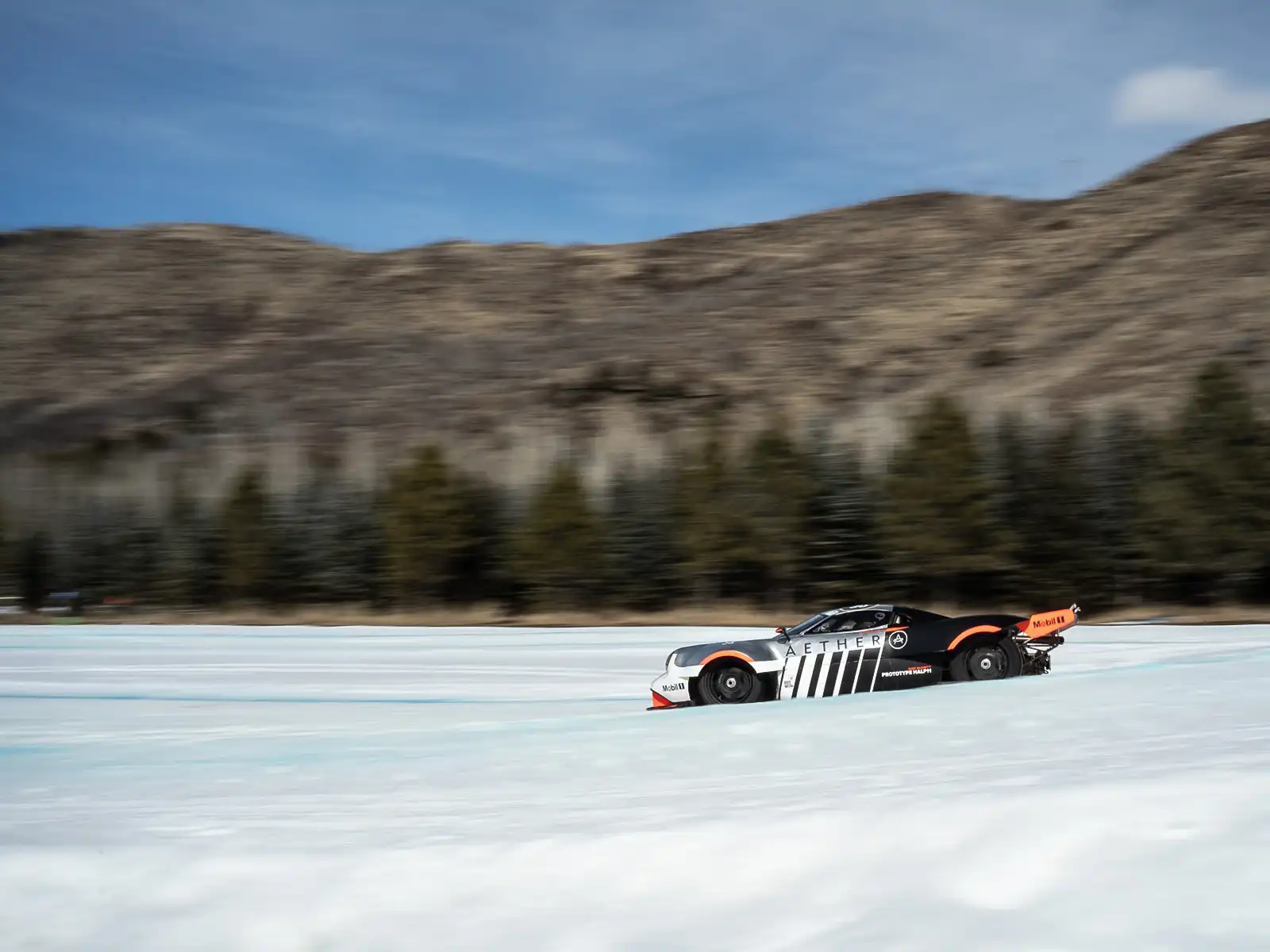 Oilstainlab’s Half11 prototype races through the snow-covered FAT Ice track, with towering mountains in the background.