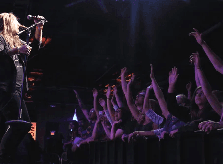 Indoor concert venue with seated audience watching artist on stage.