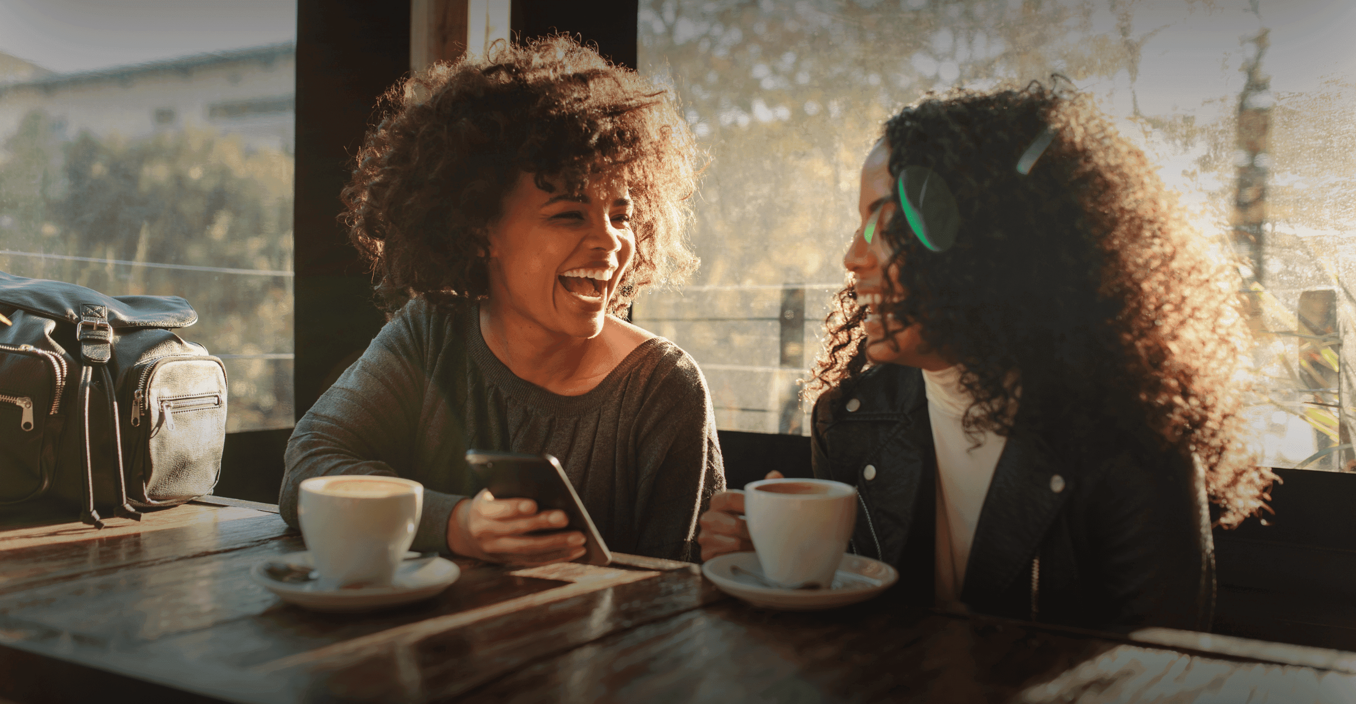 Two black women laughing whilst drinking coffee together