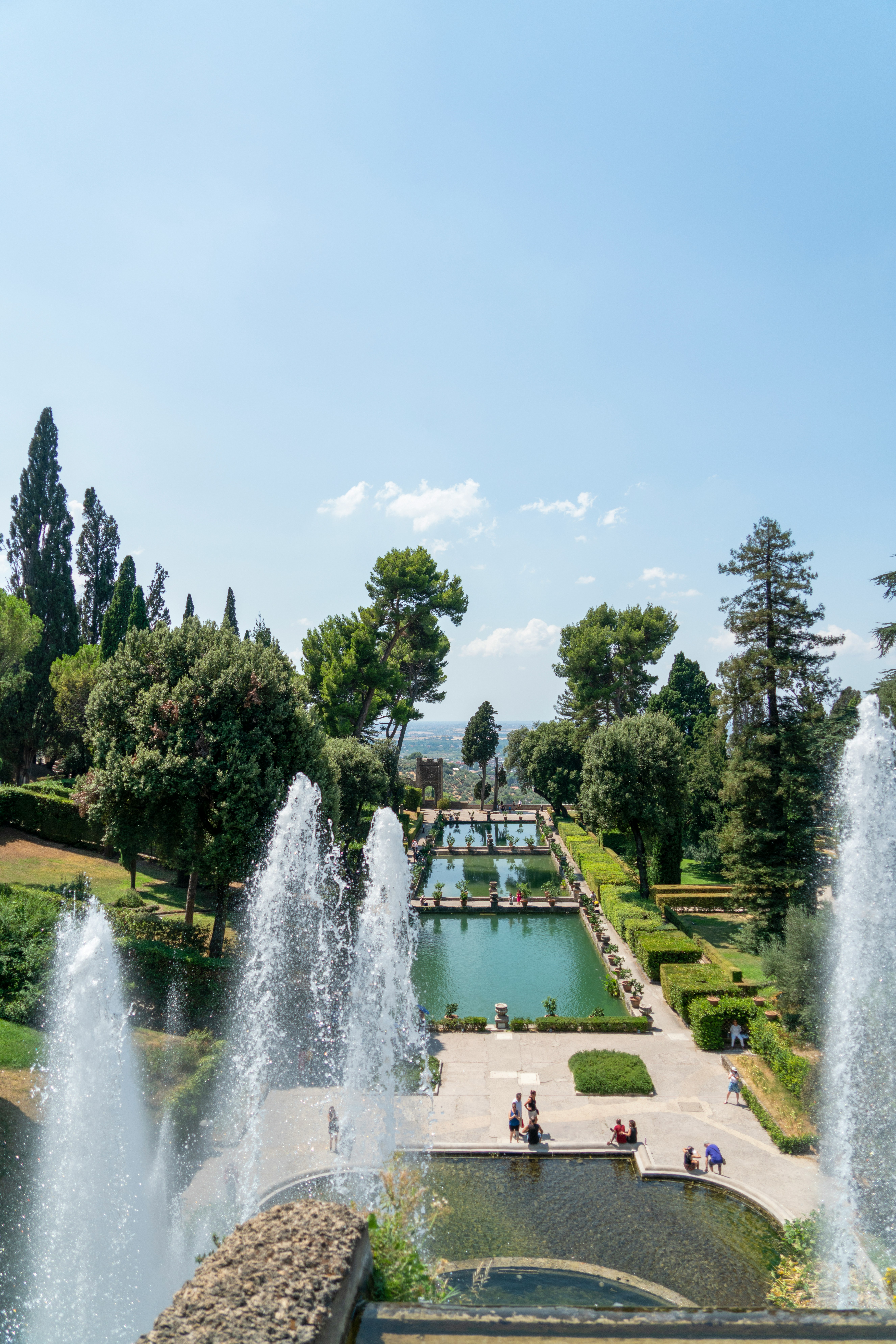 Looking across a large reflecting pool with a fountain shooting water straight up at Villa d'Este in Tivoli, Italy.