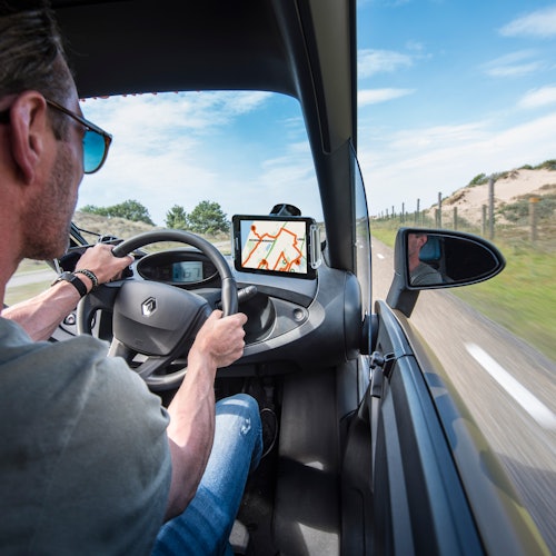 一位驾车者的导航屏幕可见，显示着地图。汽车行驶在一条公路上，旁边是沙丘和蓝天。