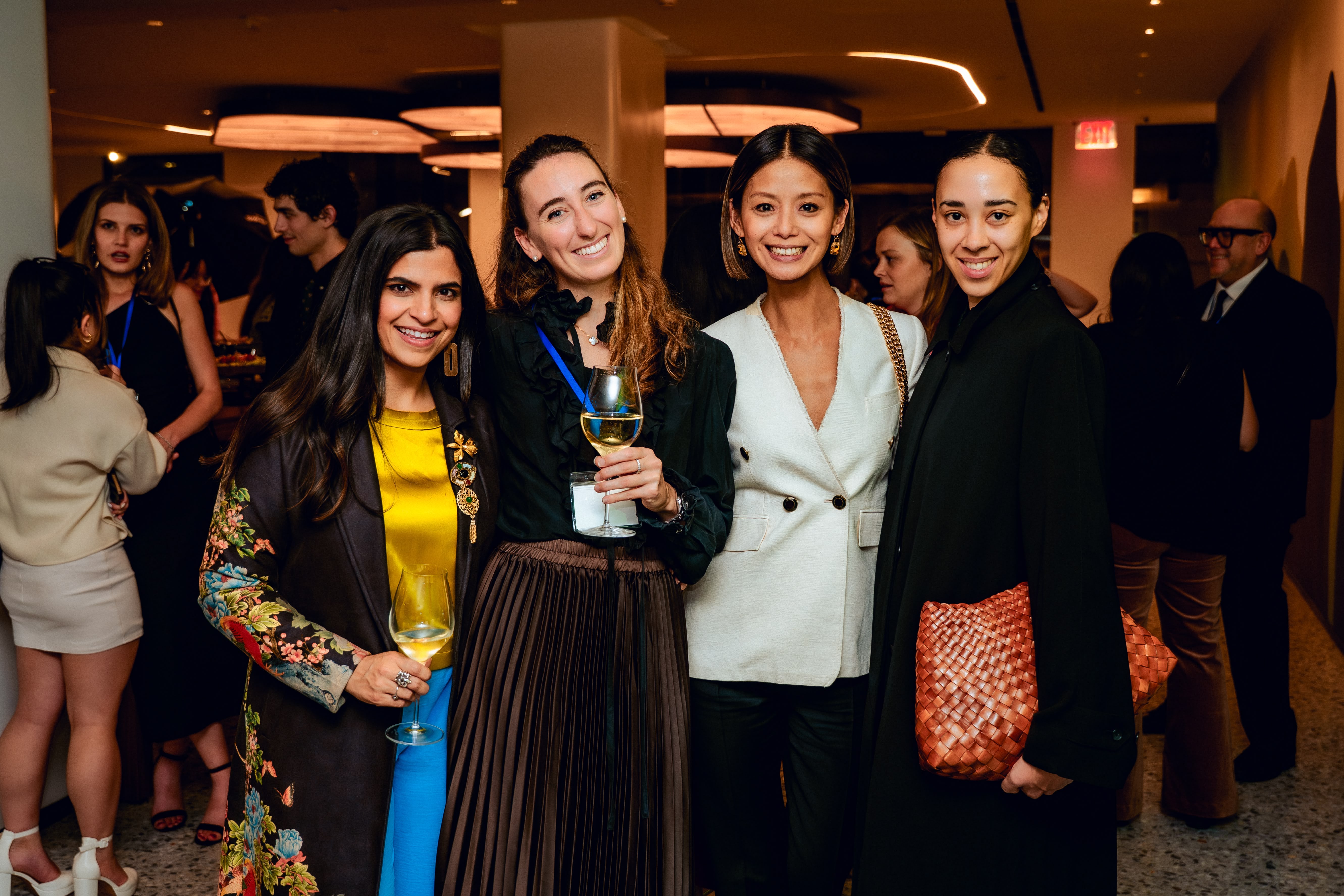 A group of five women wearing formal attire poses together at an event, smiling for the camera.