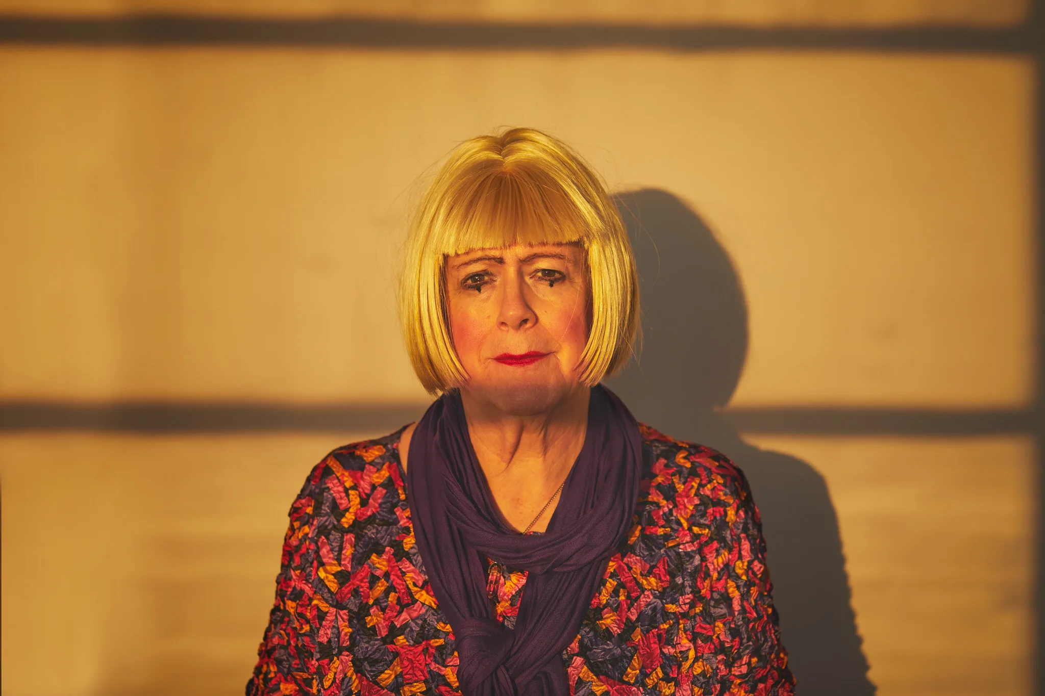 woman in blonde wig under slatted light — portrait photography by Tom Kubik