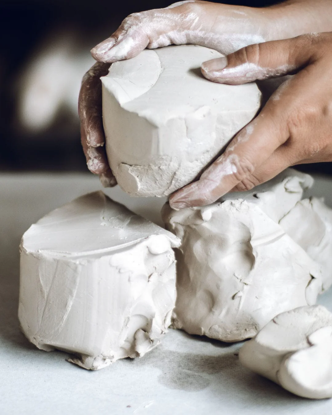 Mains enduites d'argile blanche manipulant des blocs de pâte crue dans un atelier de céramique, photographie en noir et blanc