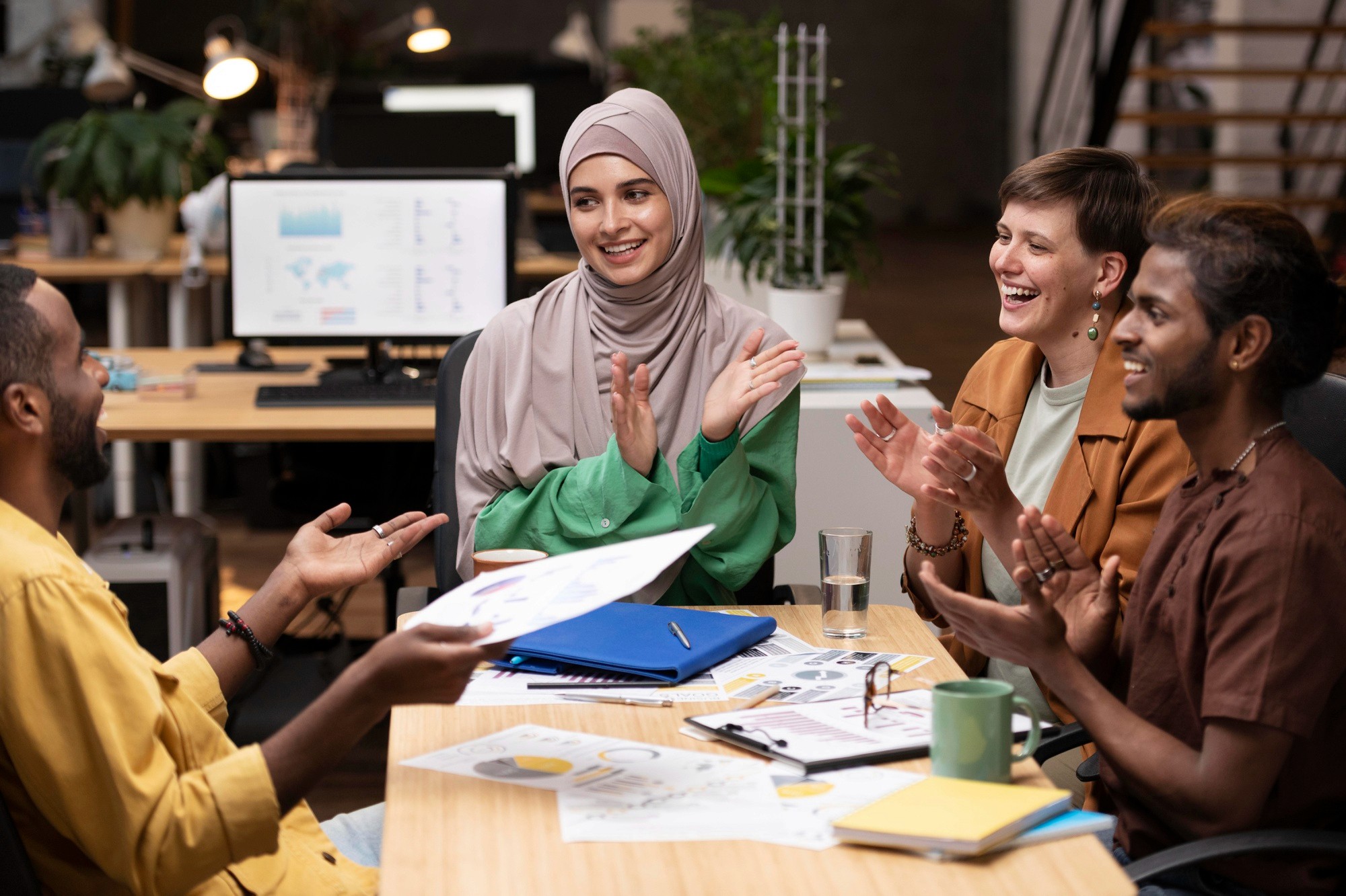 Diverse team celebrating in a modern office, clapping during a collaborative discussion.