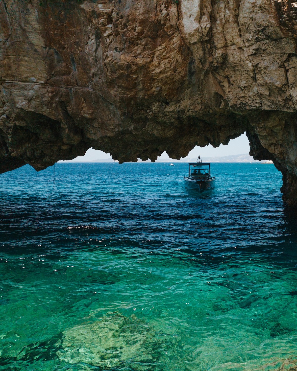Small boat viewed through a natural rock cave opening with crystal-clear turquoise waters in the Cyclades.