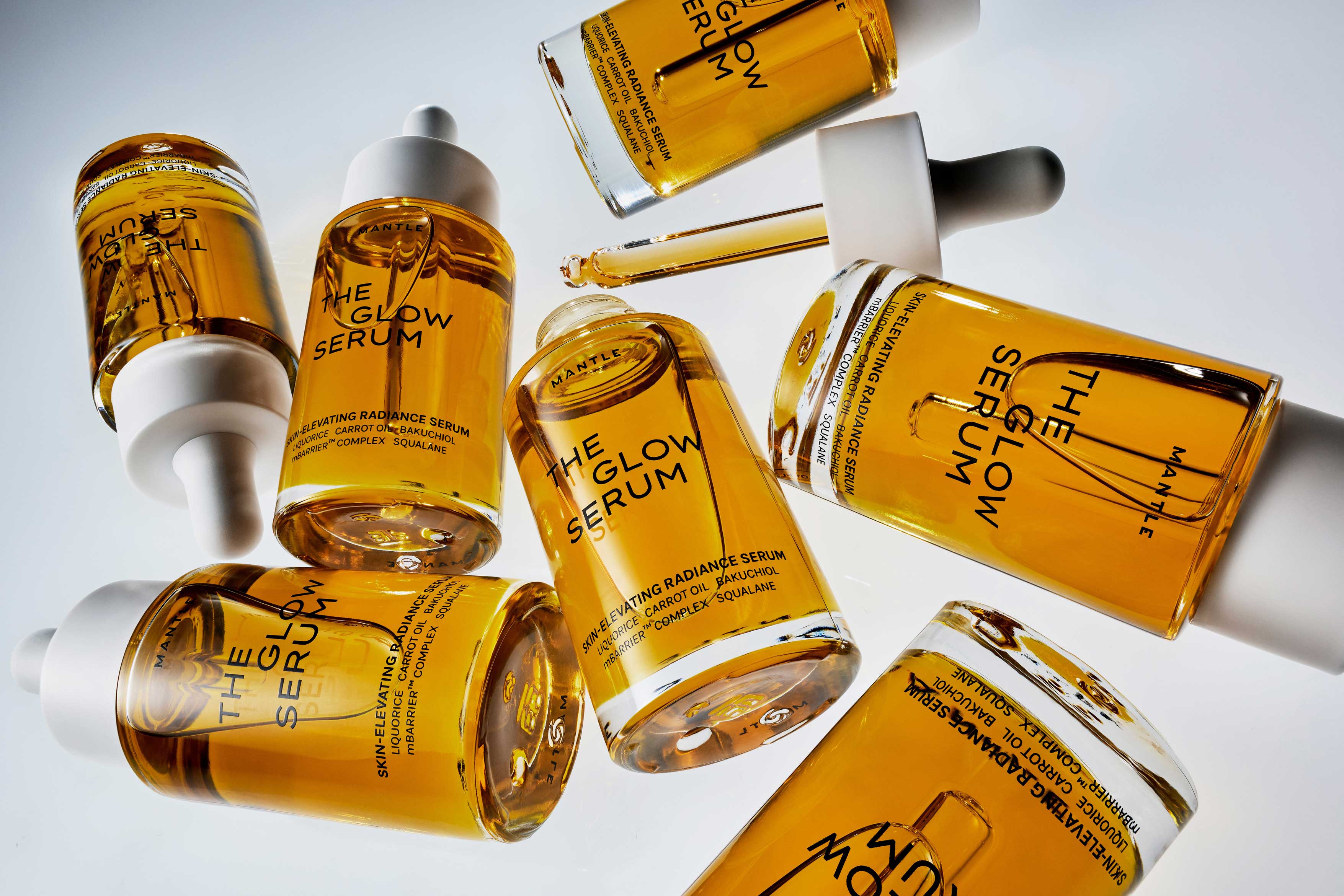 Multiple bottles of golden-yellow "The Glow Serum" by Mantle with droppers.