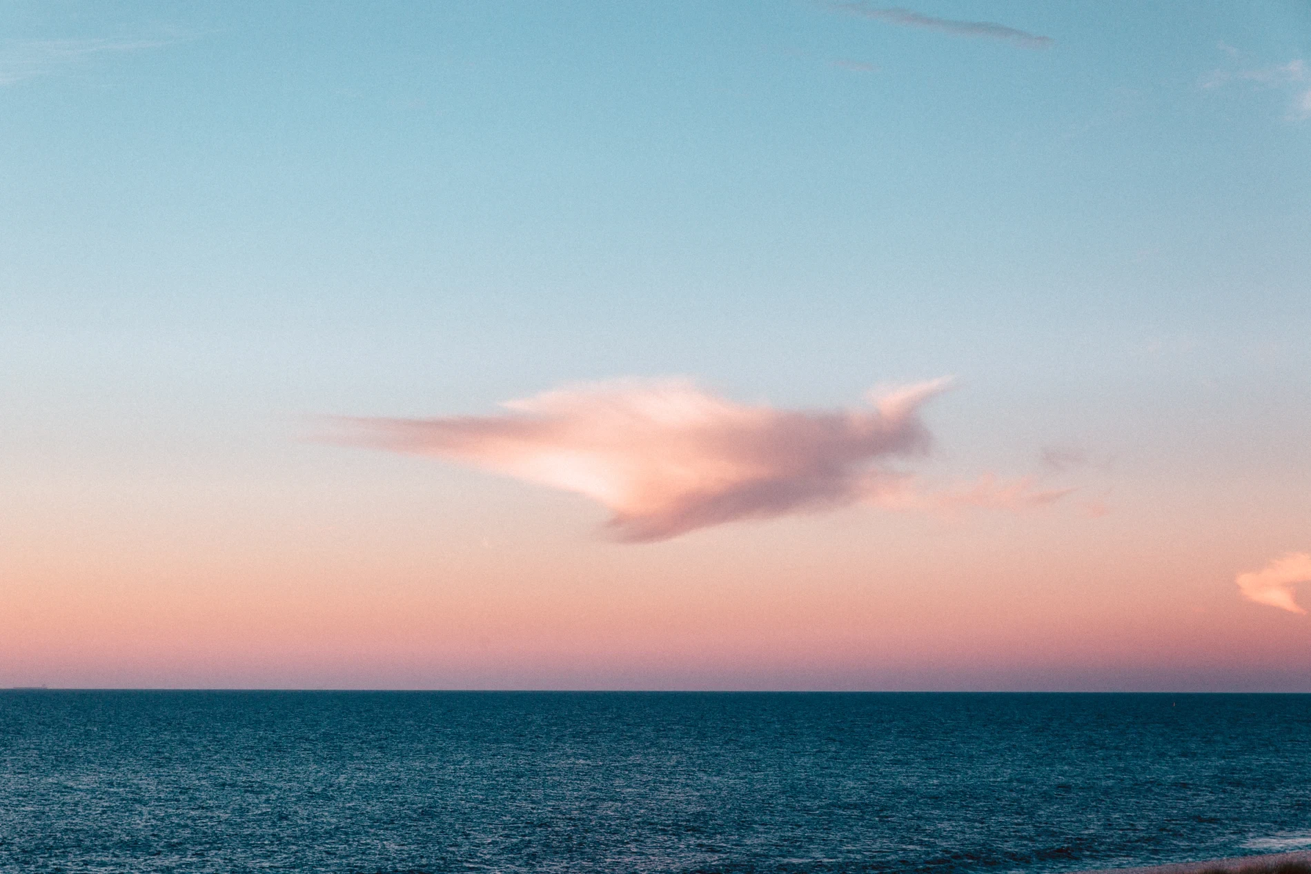 A single lit cloud over calm open ocean at dusk