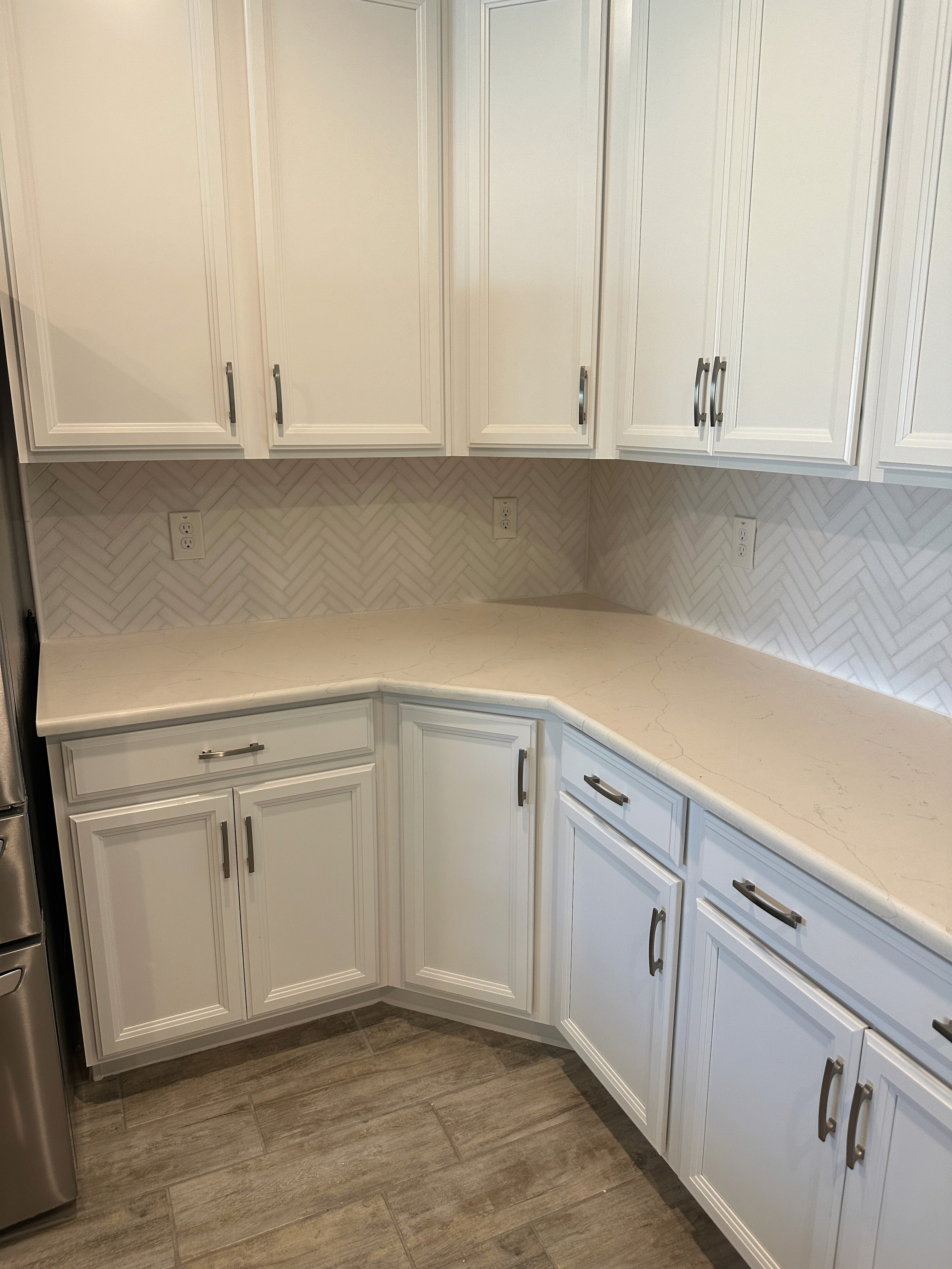 Contemporary kitchen with white cabinets, a herringbone tile backsplash, and a corner countertop design.