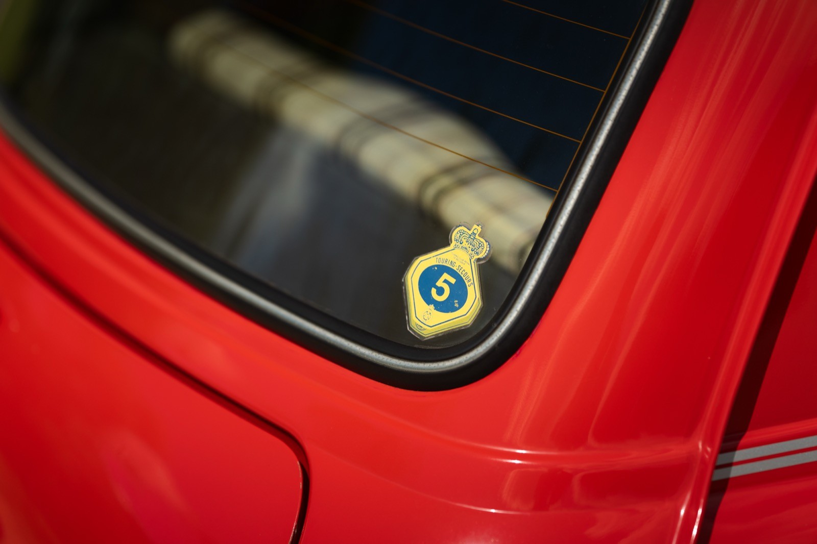 Close-up of a red car's rear window, featuring a yellow sticker with a circular design.