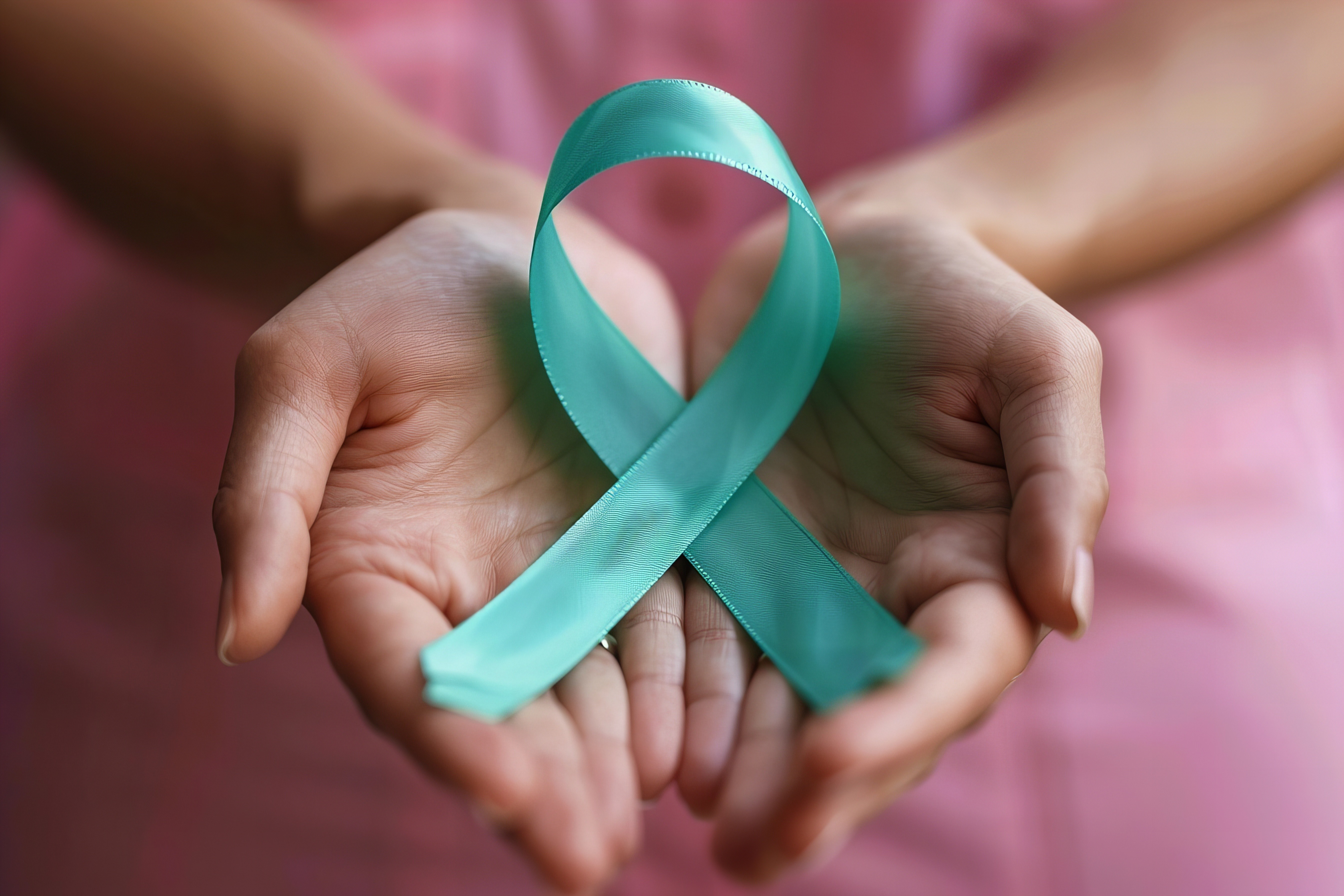 Woman dressed in pink showing only her open hands holding a turquoise cancer rippon