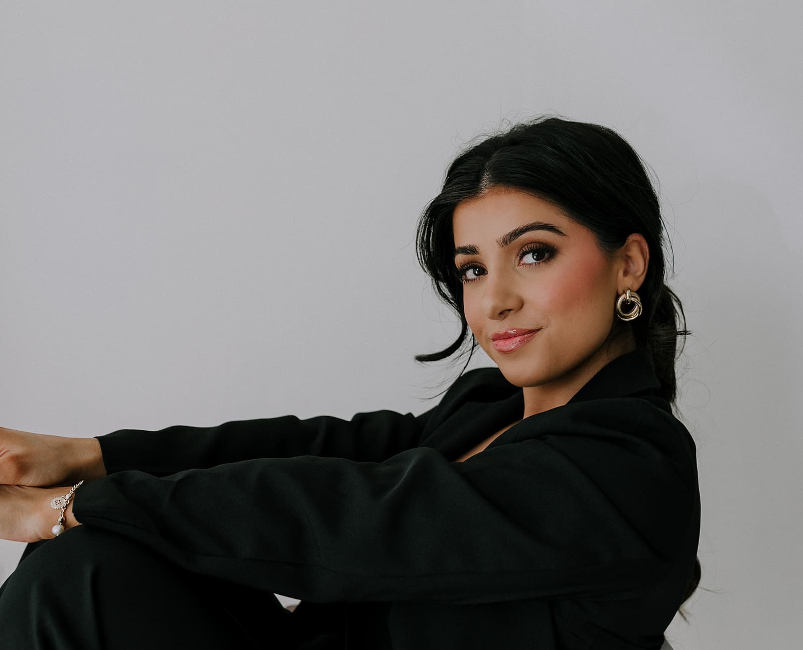 A model, Haley Gould, sits wearing a black outfit with gold earrings in a natural light studio in Shreveport.