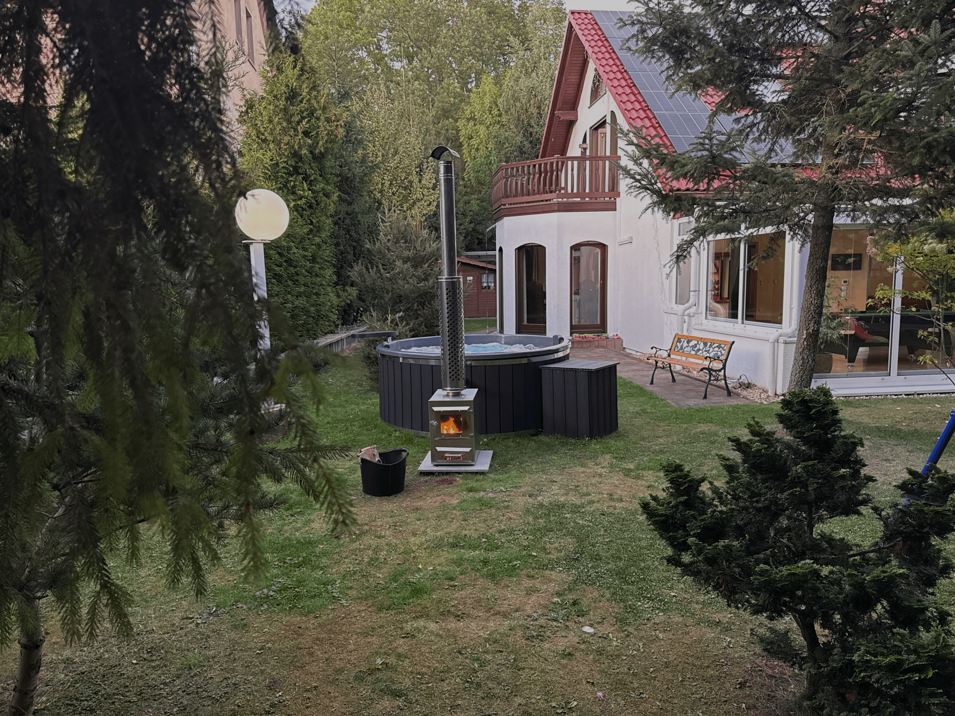 Outdoor hot tub installation with wood-fired heater in a backyard near a modern house