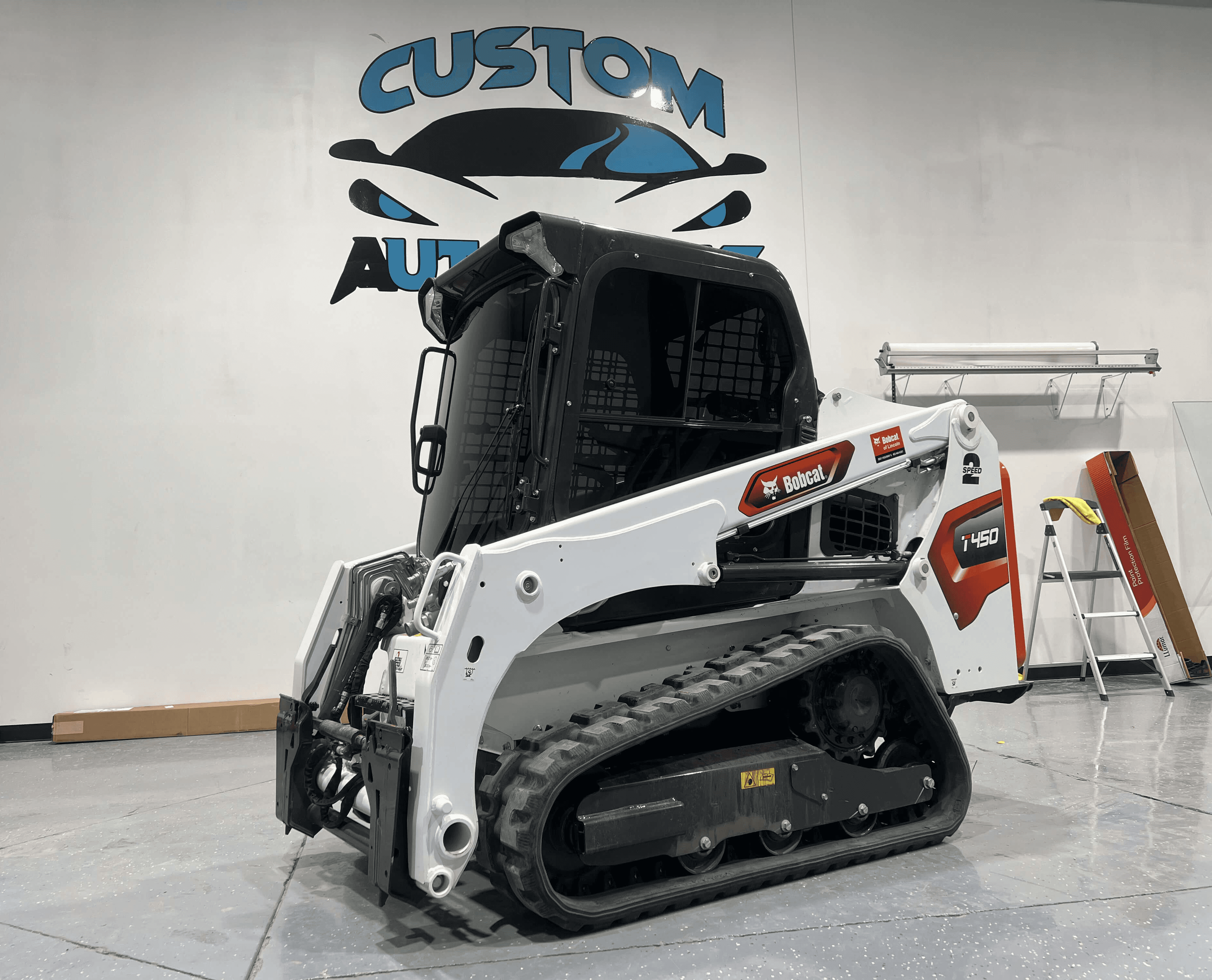 A white Bobcat T450 compact track loader is parked indoors on a polished gray floor.