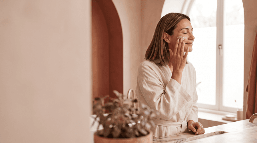 Frau trägt am Morgen eine Pflegecreme auf ihre Wange auf (KI-generiert)