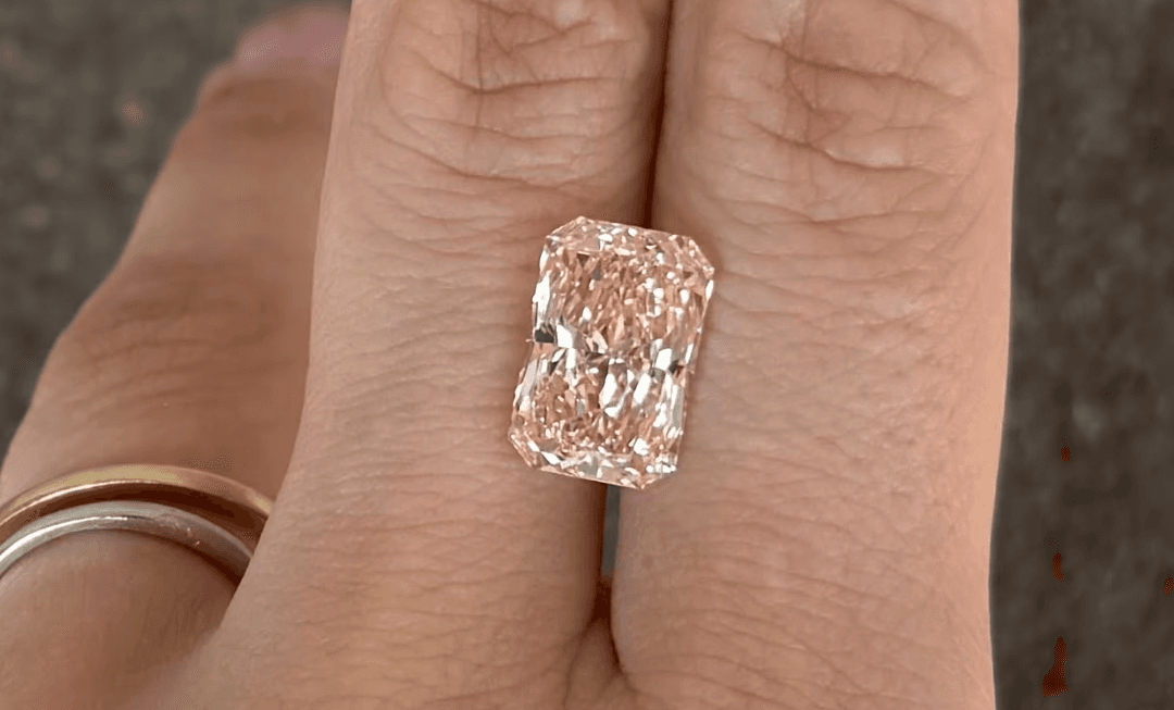 Close up of a Pink lab-grown diamond in between index and middle finger by Lab Grown Dreams.