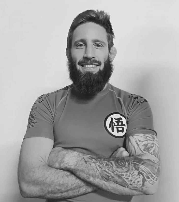 Man smiling, arms crossed. Beard, tattoo, and cauliflower ear visible. Shirt with Dragonball Z symbol.