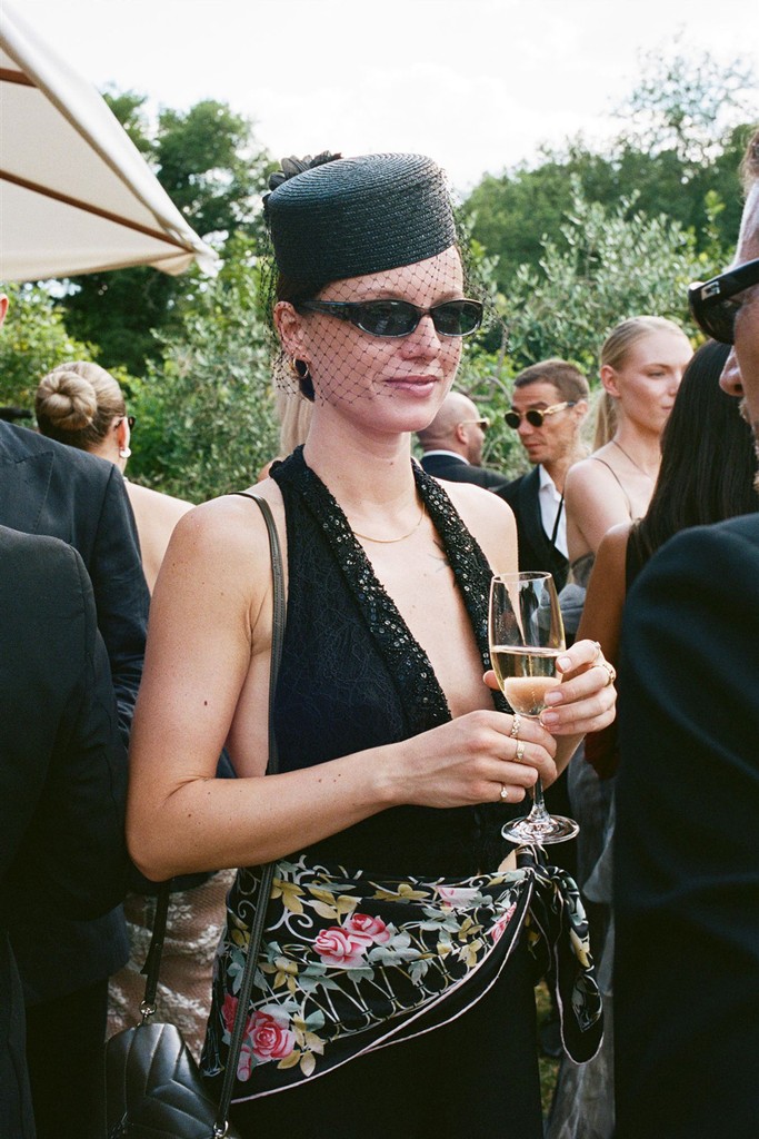 Stylish wedding guest in black attire holding a champagne glass during cocktail hour