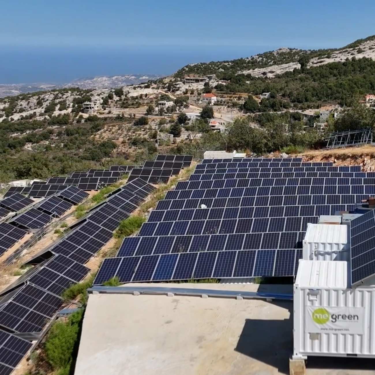 A hillside solar farm featuring rows of solar panels harnessing sunlight amidst a lush green landscape, with a clear blue sky and a distant building, showcasing renewable energy technology and sustainable development.