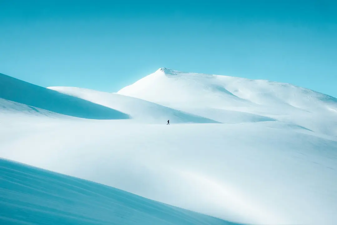 Solitary figure crossing a vast minimalist snow-covered mountain landscape, illustrating mental clarity, focus, and stripping life back to essentials