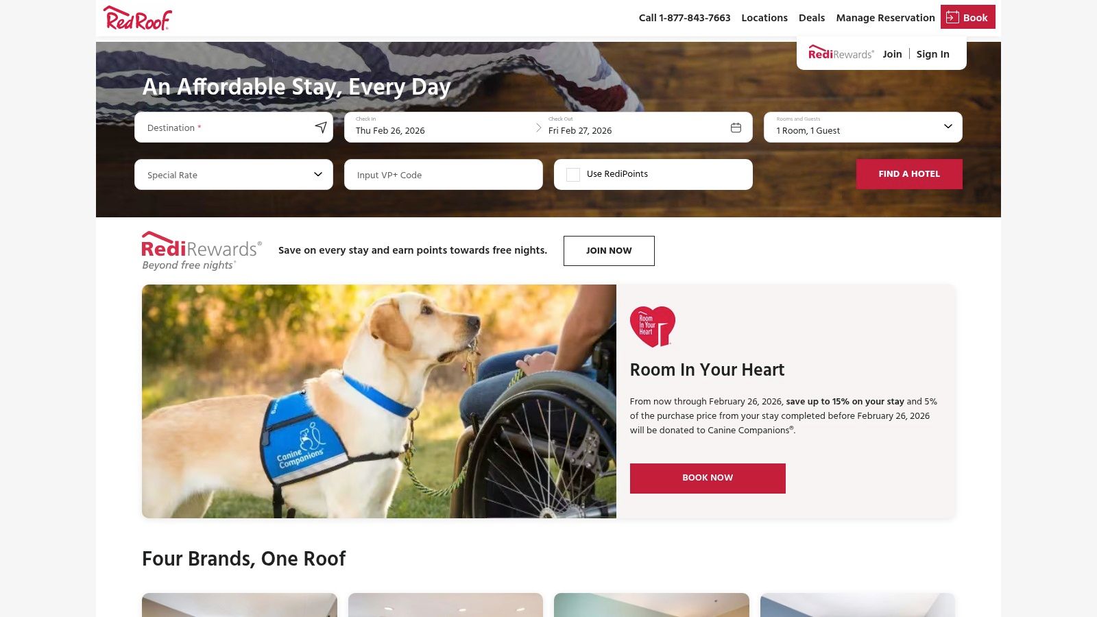 A service dog wearing a vest stands proudly next to its owner's luggage in a motel room.