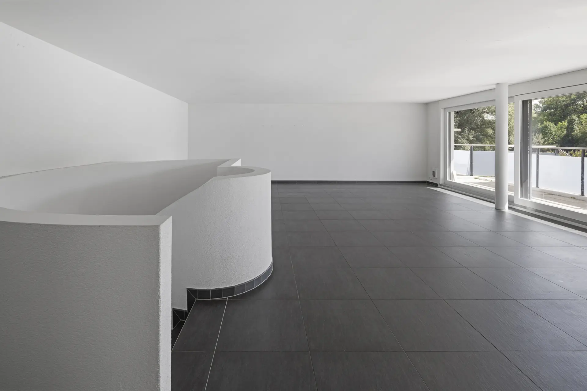 Wohnzimmerbereich mit anthrazitem Bodenbelag, Immobilienfoto.