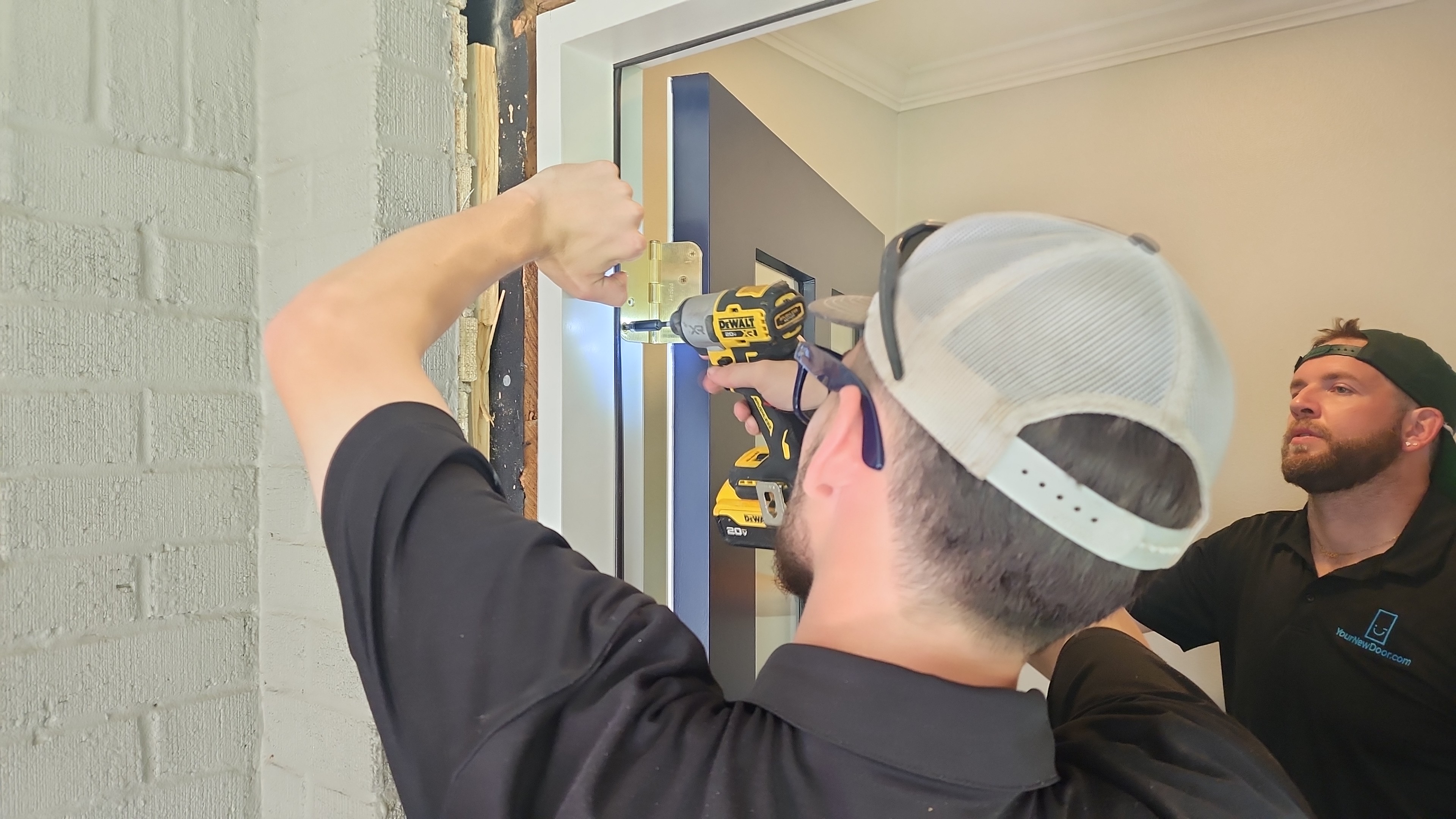 Two Your New Door technicians on a door replacement job in Dallas - Fort Worth. One of them installs the hinges on the door, while the other one looks on.