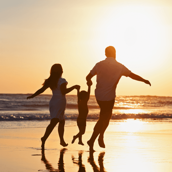 a mother, father and child playing on the beach at sunset