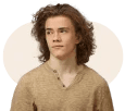 Young person with curly hair, wearing a beige shirt, looking contemplatively to the side against a light background.