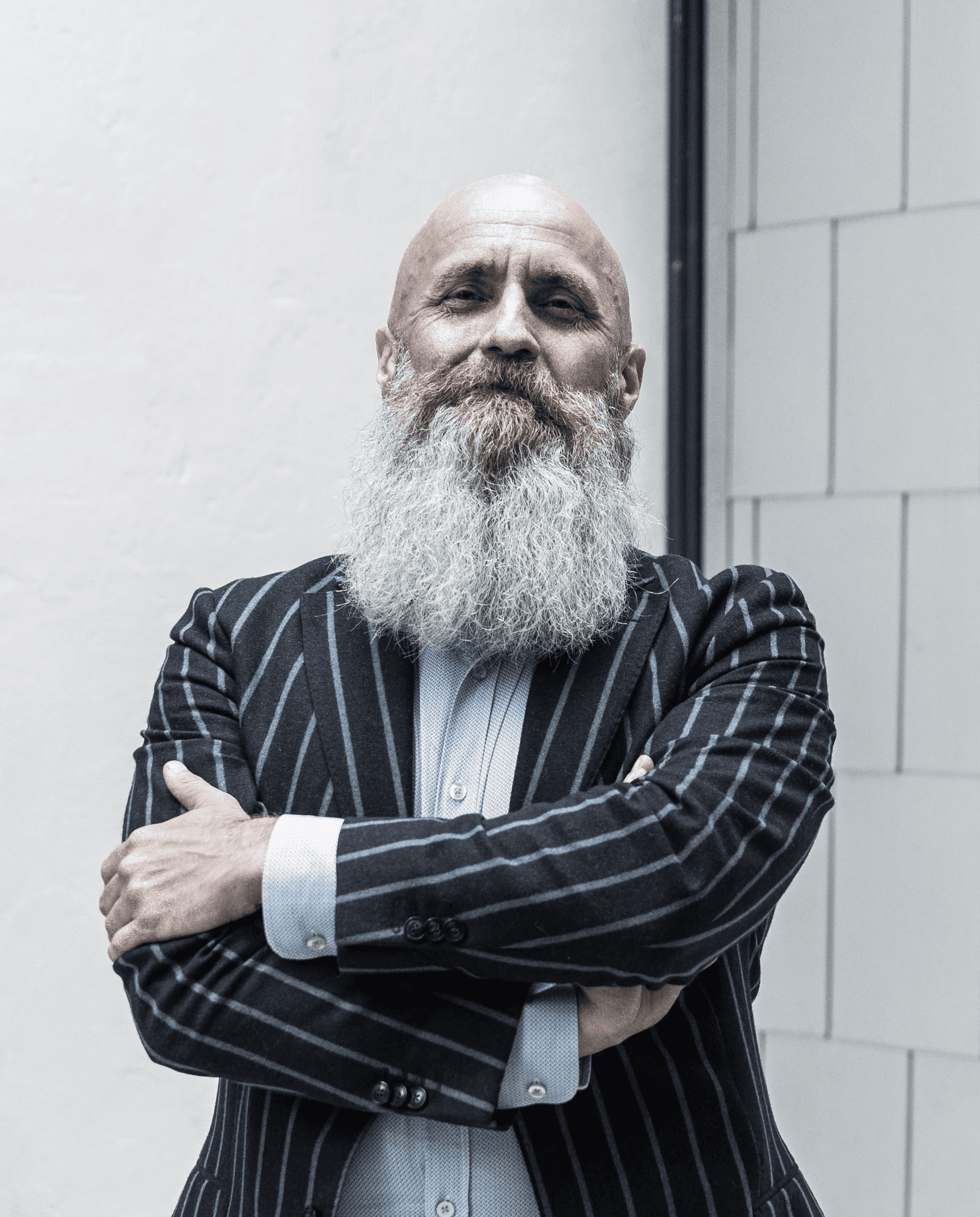 Bas Stronks, man met grijze baard en streepjespak en roze scheonen zittend in een industriele omgeving.