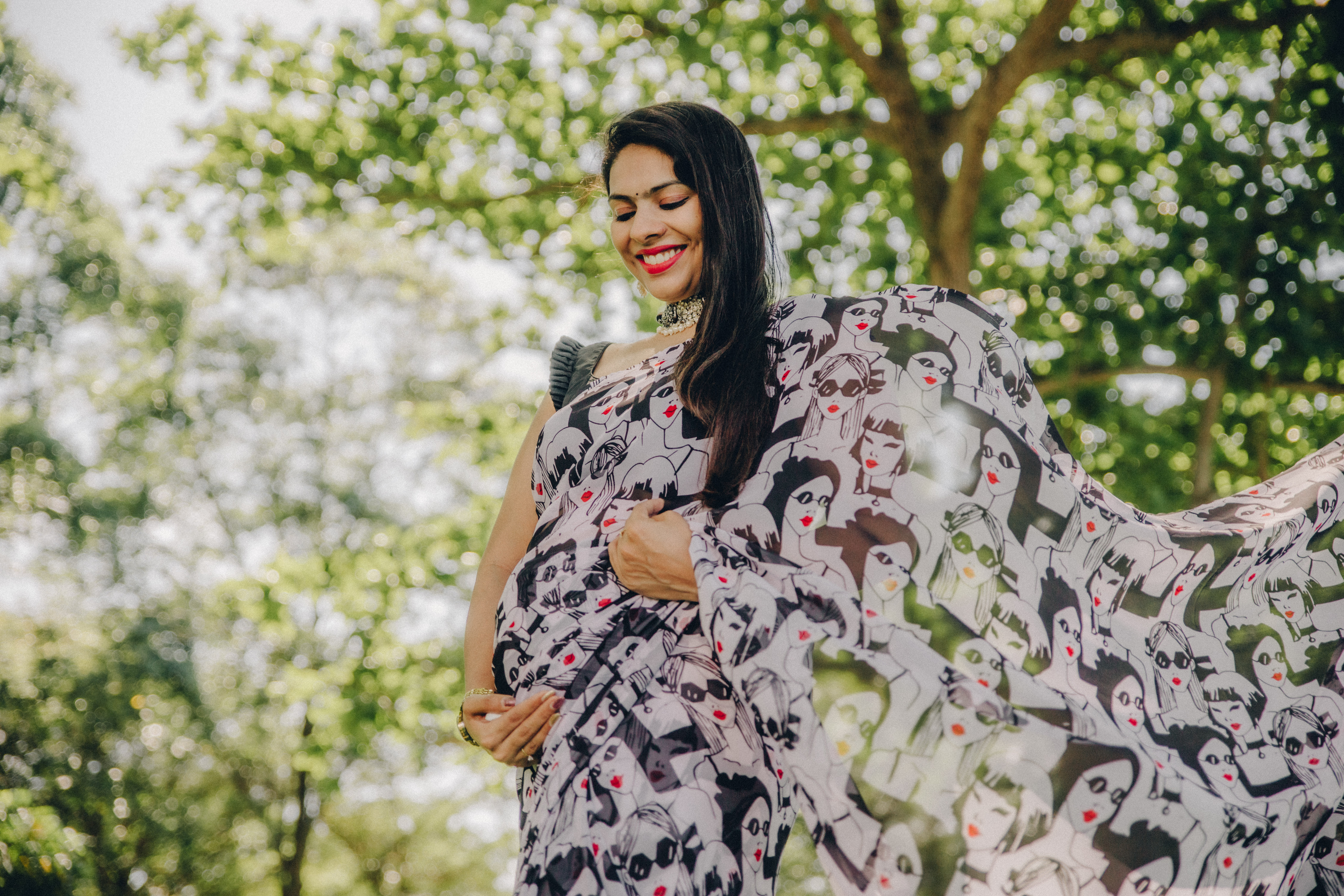 Maternity portrait of a woman glowing in a black and white abstract pattern dress, outdoors.

