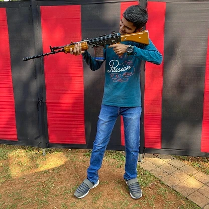 FPS gaming enthusiast posing with a tactical rifle replica at an outdoor exhibition showcase.