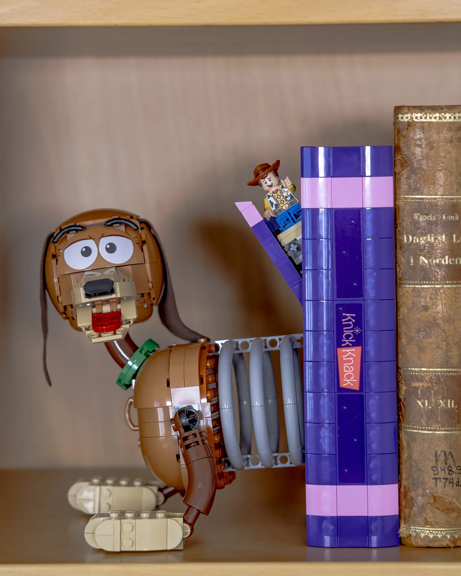 LEGO Toy Story-bokstøtte med Slinky Dog og LEGO figur av Woody som stikker frem, plassert sammen med bøker i en bokhylle