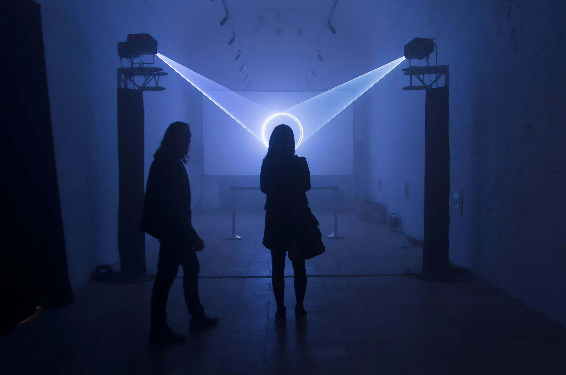 Two people observe a light installation with projectors and a circular halo.