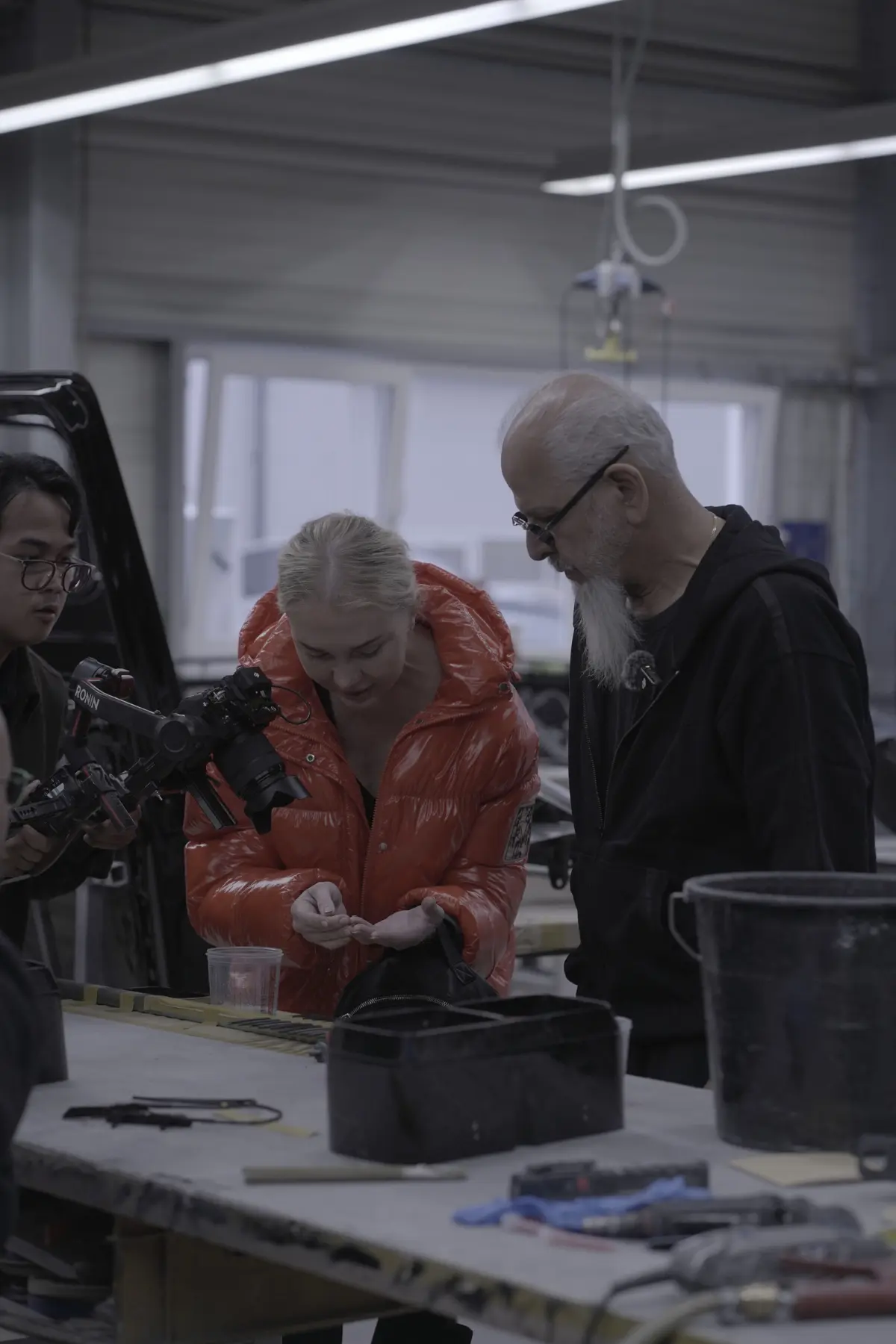 Behind the scenes filming inside the Mansory factory with Elena and Kourosh Mansory reviewing material while a cameraman records