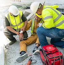 A photo of 2 men on a building site assisting a man who is on the floor