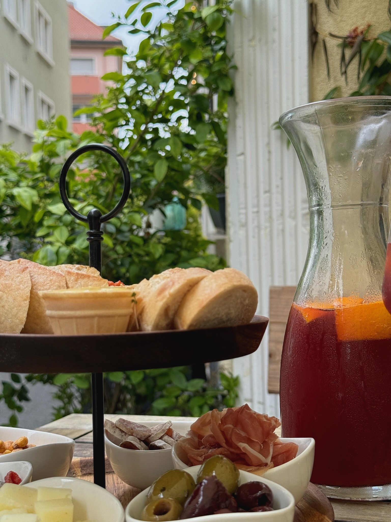 Nahaufnahme eines Tabletts mit verschiedenen Antipasti und einer Karaffe Sangria auf einem Holztisch im Freien.