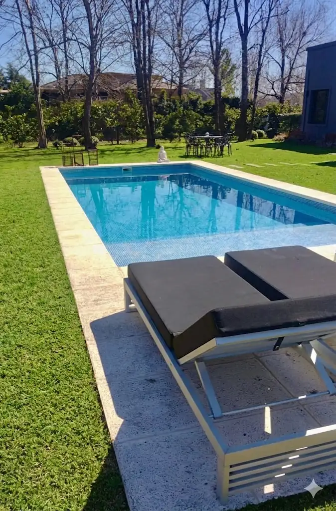 Gran pileta revestida en venecitas premium con agua turquesa, ubicada en un extenso parque arbolado con elegantes reposeras negras de diseño.