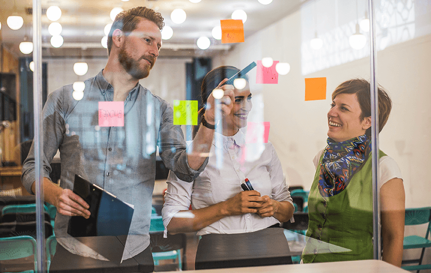 Cross-functional team collaborating with sticky notes on a glass wall, representing the strategic alignment and evidence-based design Public Works brings to complex organizational challenges