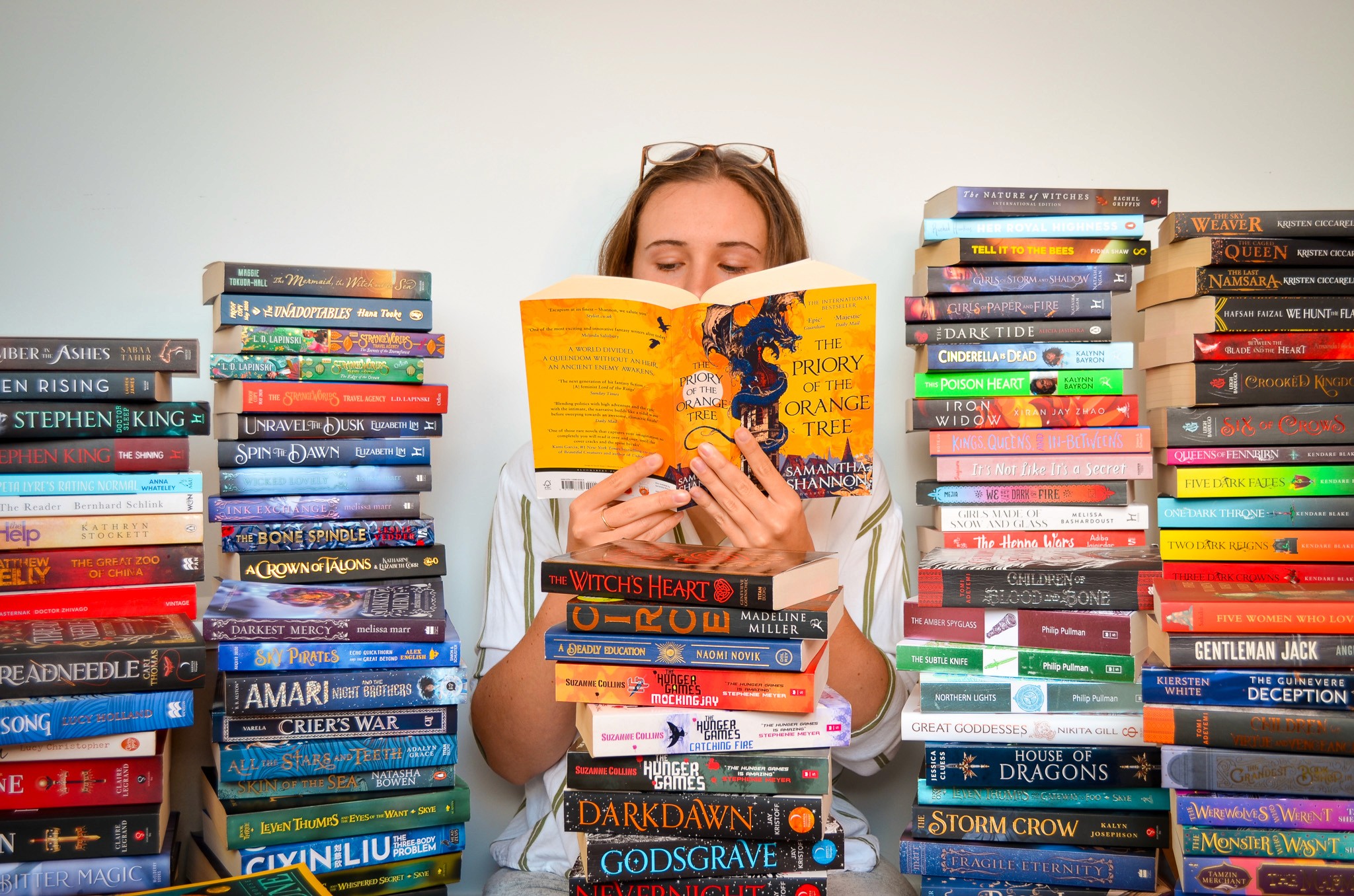 Erin Middleton sitting between stacks of fantsy books, reading The Priory of the Orange Tree.