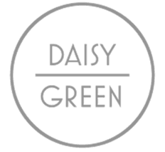 Smiling man wearing glasses and a casual blue shirt over a white t-shirt, standing in soft natural light with window shadows on a gray wall behind.