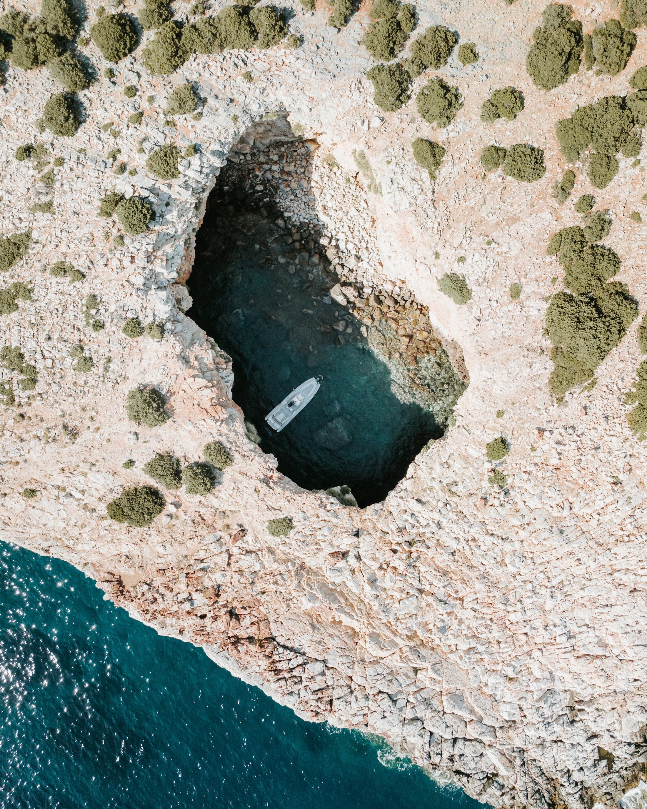 White motor yacht anchored in a secluded circular cove surrounded by dramatic limestone cliffs and Mediterranean coastline.
