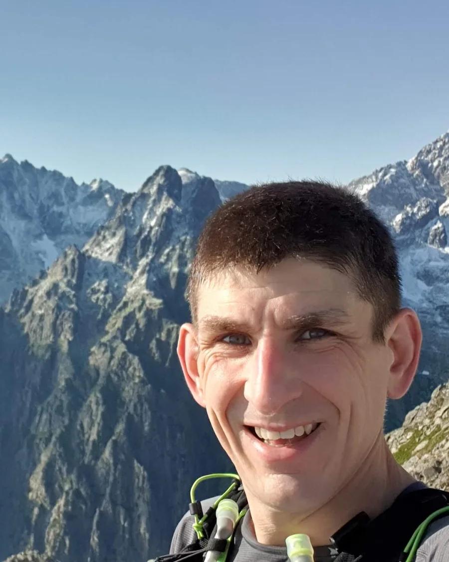 Jason Millward, smiling, wearing a running vest on a mountain ridge.